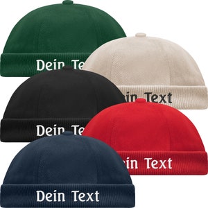Könnte beinhalten: Fünf verschiedene farbige Cord-Beanie-Mützen mit dem Text "Dein Text" auf der Vorderseite gestickt. Die Mützen sind grün, beige, schwarz, rot und marineblau.