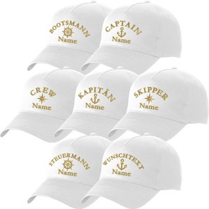 Könnte beinhalten: Sechs weiße Baseballkappen mit verschiedenen nautischen Stickereien. Die Designs beinhalten ein Schiffswheel, einen Anker und einen Kompass. Jede Kappe hat das Wort "Name" unter dem Design gestickt.