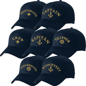 Könnte beinhalten: Sechs marineblaue Baseballkappen mit goldener Stickerei. Die Kappen zeigen nautische Motive mit Wörtern wie "Bootsmann", "Captain", "Crew", "Kapitän", "Skipper", "Steuermann" und "Wunschtext". Jede Kappe hat ein anderes nautisches Symbol, darunter ein Kompass, ein Anker und ein Steuerrad.