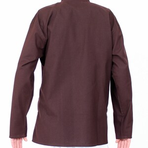 May include: A brown long-sleeved shirt with a mandarin collar. The shirt is made of a solid, dark brown fabric. The sleeves have buttoned cuffs. The shirt is shown from the back.