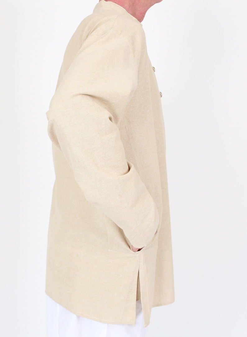 May include: A light beige long-sleeved jacket with a mandarin collar and two buttons. The jacket has two pockets and a side slit. The fabric appears to be a woven material. The jacket is worn over white pants.