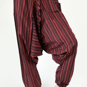 May include: Striped harem pants in shades of burgundy, red, yellow, and black. These loose-fitting pants feature a drawstring waist, pockets, and elastic cuffs at the ankles. The fabric has vertical stripes.