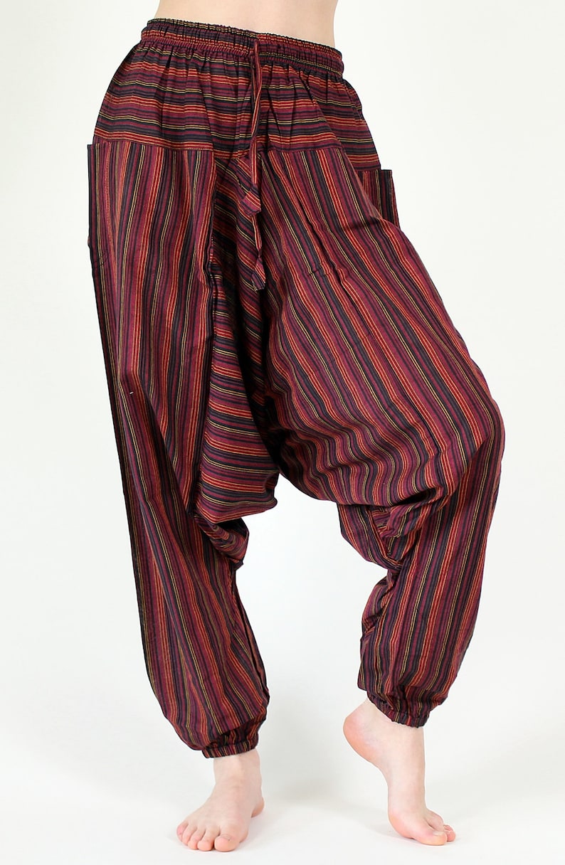 May include: Striped harem pants in shades of burgundy, red, yellow, and black. These loose-fitting pants feature a drawstring waist, pockets, and elastic cuffs at the ankles. The fabric has vertical stripes.