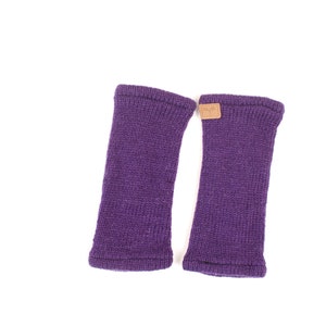 May include: A pair of purple knitted wrist warmers. Each warmer is a solid color with a ribbed cuff and a small, rectangular brown tag near the top. The warmers are designed to cover the wrist and part of the hand.