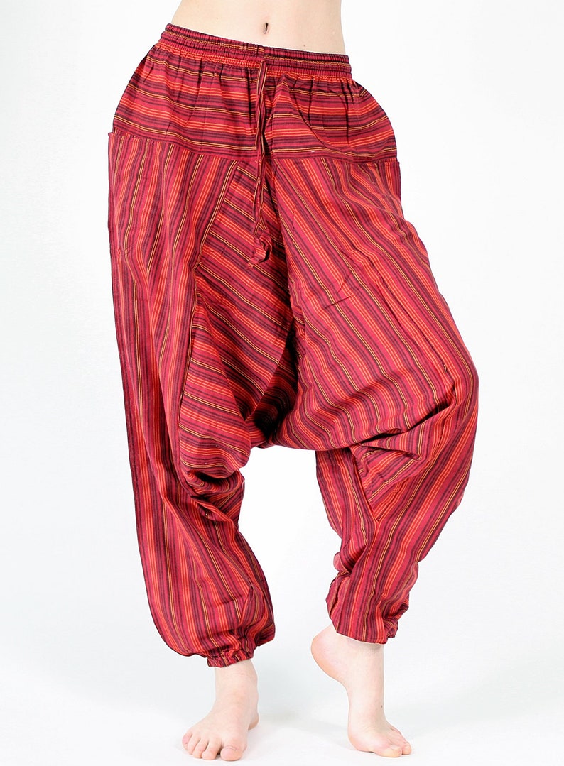 May include: Red and maroon striped harem pants with a drawstring waist and pockets. The loose-fitting pants have a gathered ankle and are made of a lightweight fabric. The vertical stripes create a visually appealing pattern.
