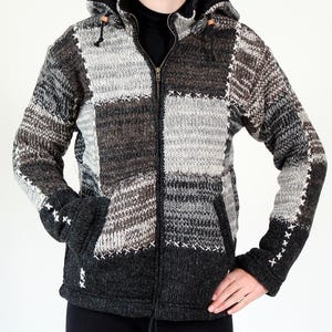 Può includere: Giacca con cappuccio patchwork nei toni del grigio, nero e marrone. La giacca presenta una cerniera intera, tasche anteriori e dettagli a punto croce bianchi. Realizzata in un materiale a maglia spesso e strutturato.