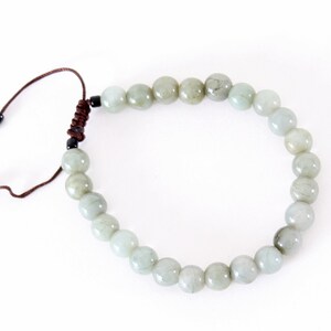 May include: A beaded bracelet featuring pale green, round beads. The bracelet is strung on a brown cord with an adjustable sliding knot closure. The beads have a smooth, polished appearance and vary slightly in color.