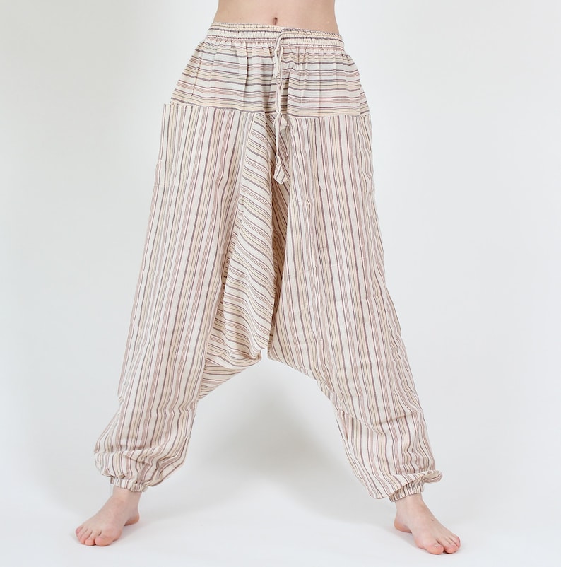 May include: Cream-colored harem pants with vertical stripes in shades of brown and red. The pants have a drawstring waist and elastic cuffs at the ankles. The loose, comfortable design is ideal for casual wear.
