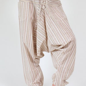 May include: Striped harem pants in beige, brown, and white. The pants have a drawstring waist and elastic cuffs at the ankles. The fabric has a vertical stripe pattern. The pants are loose-fitting and comfortable.