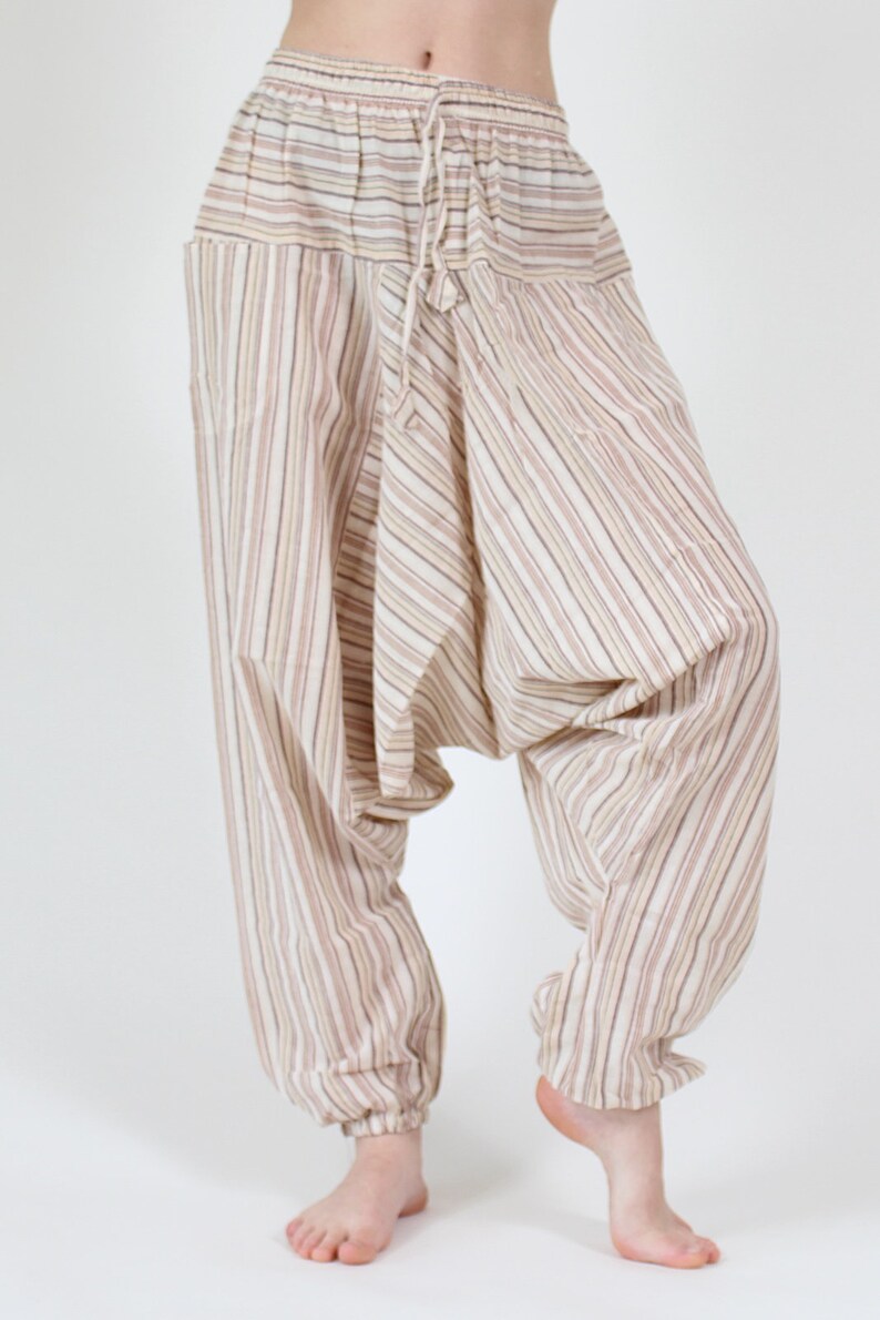 May include: Striped harem pants in beige, brown, and white. The pants have a drawstring waist and elastic cuffs at the ankles. The fabric has a vertical stripe pattern. The pants are loose-fitting and comfortable.