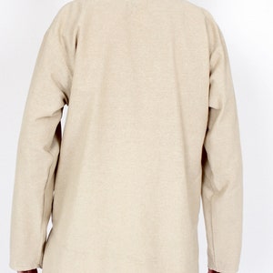 May include: A beige long-sleeved tunic with a mandarin collar. The tunic is made of a textured fabric and has a relaxed fit. The back view shows the full length of the tunic, which extends to the mid-thigh.