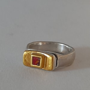 Może przedstawiać: Pierścionek srebrny i złoty z kwadratowym czerwonym kamieniem szlachetnym w środku.