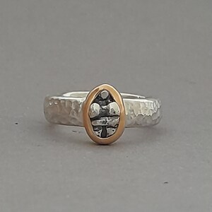 Op de afbeelding: Een zilveren ring met een gehammerde textuur en een ovale gouden zetting met een zwart-wit ontwerp.
