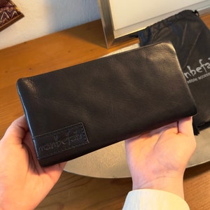 May include: Black leather wallet with a small embossed logo that says "manbefair" on the front.