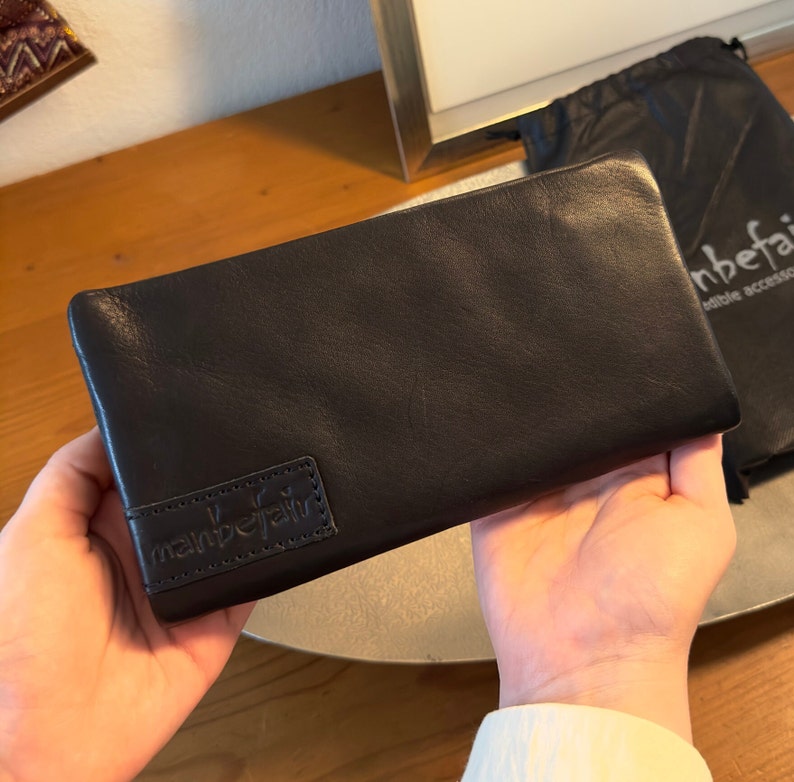 May include: Black leather wallet with a small embossed logo that says "manbefair" on the front.