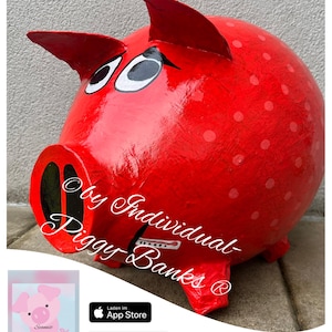 Peut inclure: Tirelire en forme de cochon rouge avec des pois blancs et des yeux noirs. La tirelire est en papier mâché et a une fente pour les pièces de monnaie sur le côté. Le texte "by Individual- Piggy Banks®" est écrit sur le côté de la tirelire.