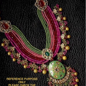 May include: A multi-strand necklace with green, pink, and red beads. The necklace has a large, green pendant with gold accents and a floral design. The pendant is surrounded by smaller beads and charms.