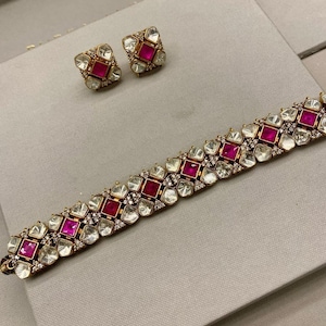 Puede incluir: Un collar y pendientes de oro con piedras rosas y blancas. El collar es una cadena delicada con un patrón repetido de piedras cuadradas y en forma de lágrima.