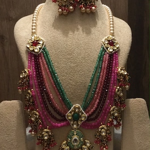 May include: A multi-strand necklace with pink, green, and red beads. The necklace has a large pendant with a green and gold design. The necklace is paired with matching earrings.