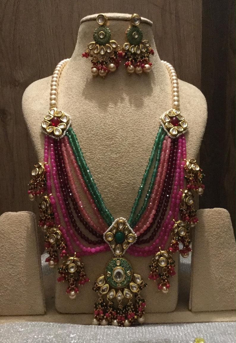 May include: A multi-strand necklace with pink, green, and red beads. The necklace has a large pendant with a green and gold design. The necklace is paired with matching earrings.