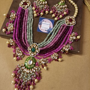 May include: A multi-strand necklace with pink, green, and white beads. The necklace has a large, ornate pendant with a green and gold design. The necklace is accompanied by a pair of matching earrings.