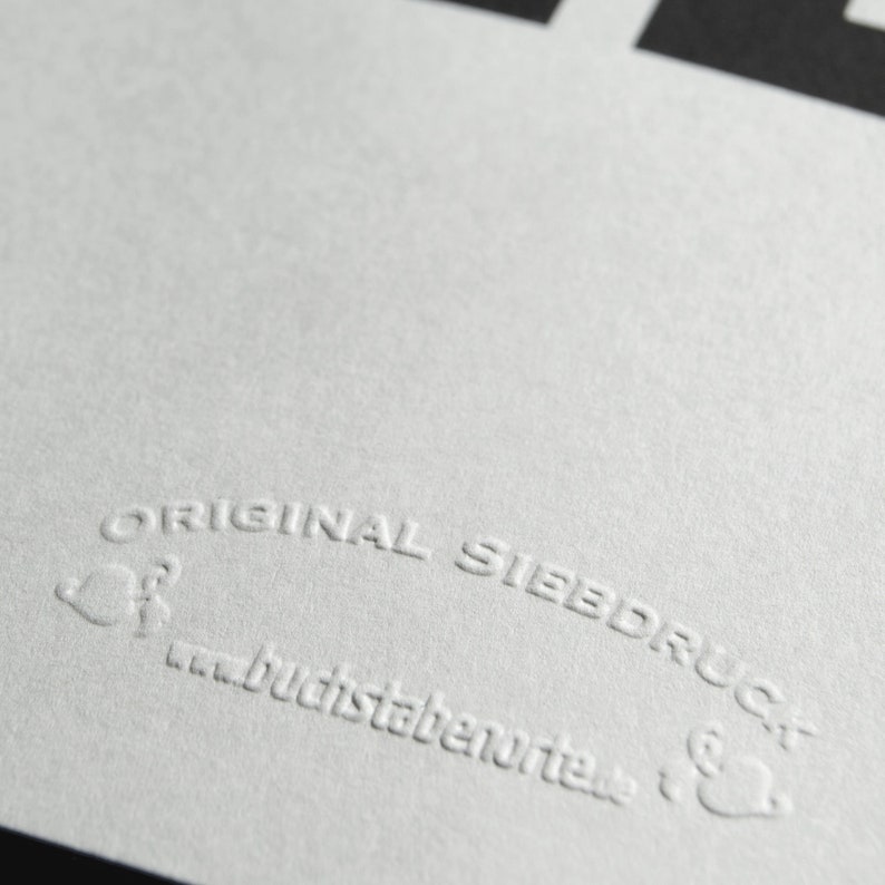 May include: Close-up of a white, textured surface with the text "ORIGINAL SIEBDRUCK" and the website address "buchstabenorte.de" embossed in the surface.