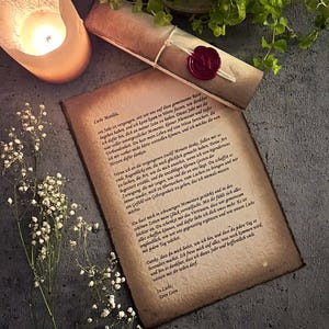 Könnte beinhalten: Romantische Szene mit einer brennenden Kerze in einem Halter, einem handgeschriebenen Brief und einer gerollten Schriftrolle, die mit rotem Wachs versiegelt ist. Zarte weiße Blumen und Grünzeug ergänzen die Komposition. Der Text des Briefes ist auf Deutsch.