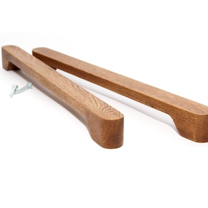 May include: Two wooden cabinet pulls with a rounded rectangular shape. The pulls are made of light brown wood with a natural grain pattern.