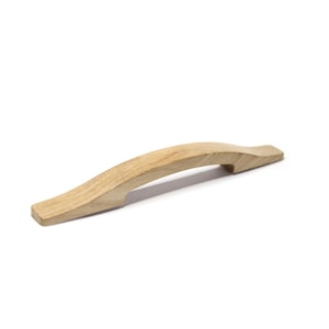 May include: A light-colored wooden cabinet handle with a curved design. The handle is made of solid wood and has a smooth, natural finish. The handle is designed for easy gripping and pulling.