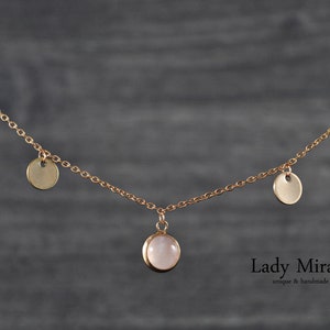 Puede incluir: Un delicado collar de cadena dorada con un colgante de piedra rosa y cuatro discos dorados más pequeños que cuelgan de la cadena. El collar está sobre un fondo gris. El texto "Lady Mirage unique & handmade" está en la parte inferior de la imagen.