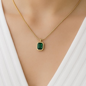 Op de afbeelding: Een gouden ketting met een groene smaragdgroene hanger.