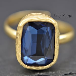 Peut inclure: Une bague en or avec une grande pierre précieuse facetée bleu foncé sertie dans un sertissage en or texturé. La bague est faite à la main et unique.