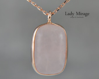 Può includere: Una collana con un ciondolo in quarzo rosa e una catena d'oro. Il ciondolo ha una forma rettangolare con una superficie liscia e lucida. Il testo "Lady Mirage unique & handmade" è visibile nell'immagine.