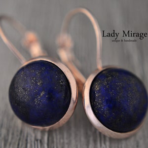 May include: Rose gold earrings with a round blue lapis lazuli stone. The earrings are handmade and unique. "Lady Mirage" is written on the image.