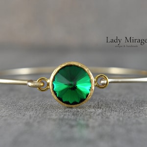 May include: A gold bangle bracelet with a single, large, round, green gemstone. The bracelet is open and has a clasp.