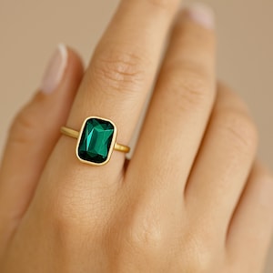 Könnte beinhalten: Ein goldener Ring mit einem großen, rechteckigen, smaragdgrünen Edelstein.