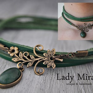 Op de afbeelding: Een groene leren choker ketting met een bronzen bloemenhanger en een groene edelsteen. De ketting is gelaagd en heeft een sluiting. De tekst "Lady Mirage unique & handmade" is zichtbaar onderaan de afbeelding.