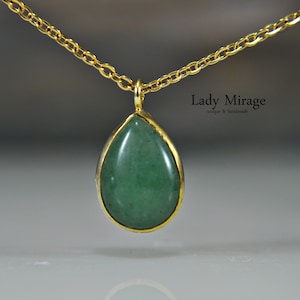 Peut inclure: Un collier en chaîne dorée avec un pendentif en forme de larme orné d'une pierre précieuse verte. Le pendentif est serti d'or et présente une finition lisse et polie. Le texte "Lady Mirage unique & handmade" est visible sur l'image.