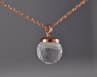May include: A delicate rose gold chain necklace with a clear faceted crystal pendant.