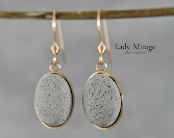 May include: A pair of gray stone earrings with gold settings. The earrings are oval shaped and have a rough, textured surface. The earrings are hanging from gold hooks.