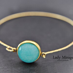 May include: A gold chain bracelet with a turquoise blue cabochon gemstone. The bracelet is delicate and features a simple design. The text "Lady Mirage unique & handmade" is visible in the image.