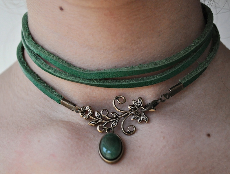 Op de afbeelding: Een groene leren choker ketting met een bronzen hanger met een gestileerd bloemmotief en een groene edelsteen.