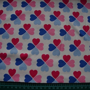 Könnte beinhalten: Weißer Stoff mit einem sich wiederholenden Muster aus rosa, blauen und roten vierblättrigen Kleeblättern.