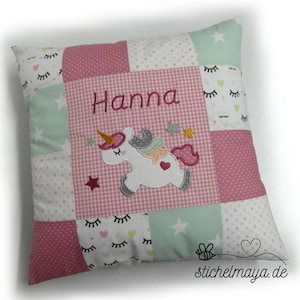 Könnte beinhalten: Ein rosa-grünes Patchwork-Kissen mit einem Einhorn und dem Namen "Hanna" bestickt.