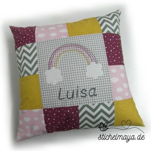 Könnte beinhalten: Ein Patchwork-Kissen mit Regenbogen- und Wolkenmuster, mit dem Namen "Luisa". Das Kissen hat eine Vielzahl von Stoffmustern, darunter Punkte, Chevron und Vichy, in den Farbtönen Rosa, Gelb, Grau und Burgunderrot.