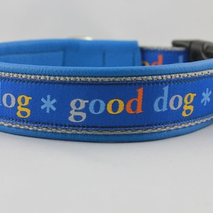 May include: A blue dog collar with the words "good dog" in colorful lettering. The collar has a padded interior and a silver metal ring for leash attachment. The collar is approximately 1 inch wide.