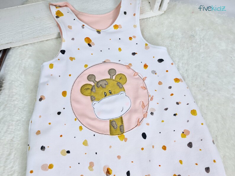 May include: A white sleeveless onesie with a pink and yellow giraffe applique. The onesie has a white background with small yellow and pink spots.