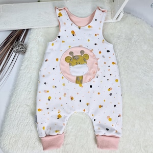 May include: White baby onesie with a pink giraffe print and a pink and white polka dot pattern. The onesie has a pink trim around the neck and leg openings.