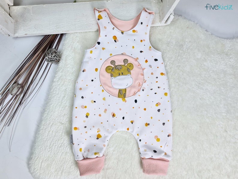May include: White baby onesie with a pink giraffe print and a pink and white polka dot pattern. The onesie has a pink trim around the neck and leg openings.