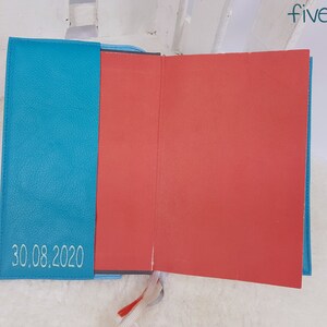 Puede incluir: Un diario de tapa dura de color azul turquesa con interior rojo y la fecha "30.08.2020" bordada en la portada.